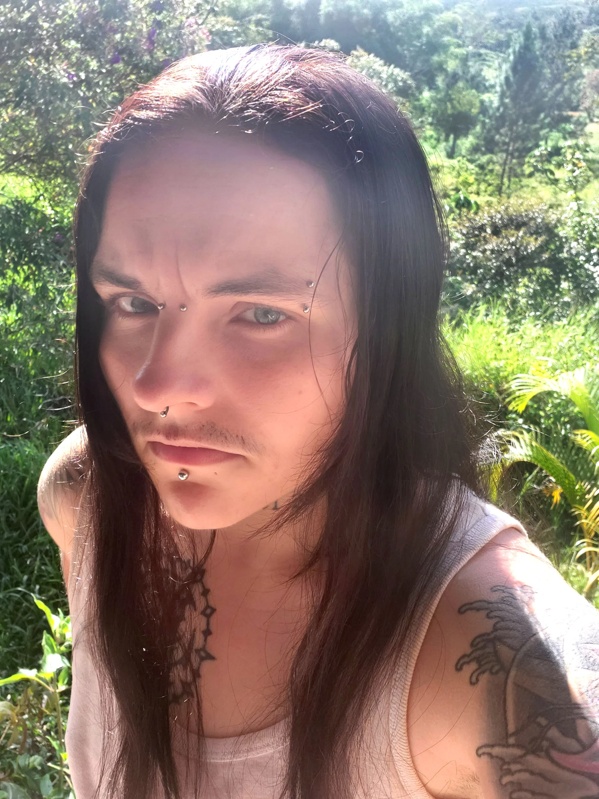 A trans man with long black hair, piercings, and tattoos.