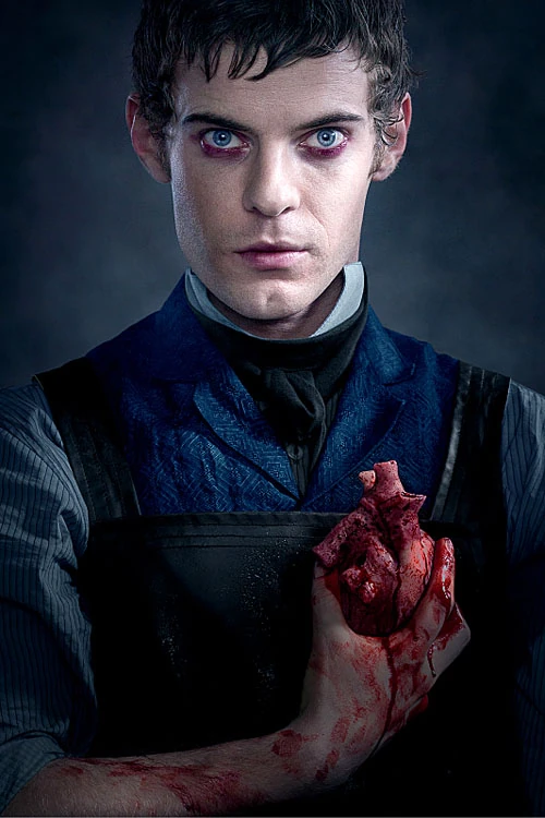 Harry Treadaway as Victor Frankenstein in Penny Dreadful, a young man with short hair and blue eyes, dressed in Victorian attire and a leather apron, holding a human heart.